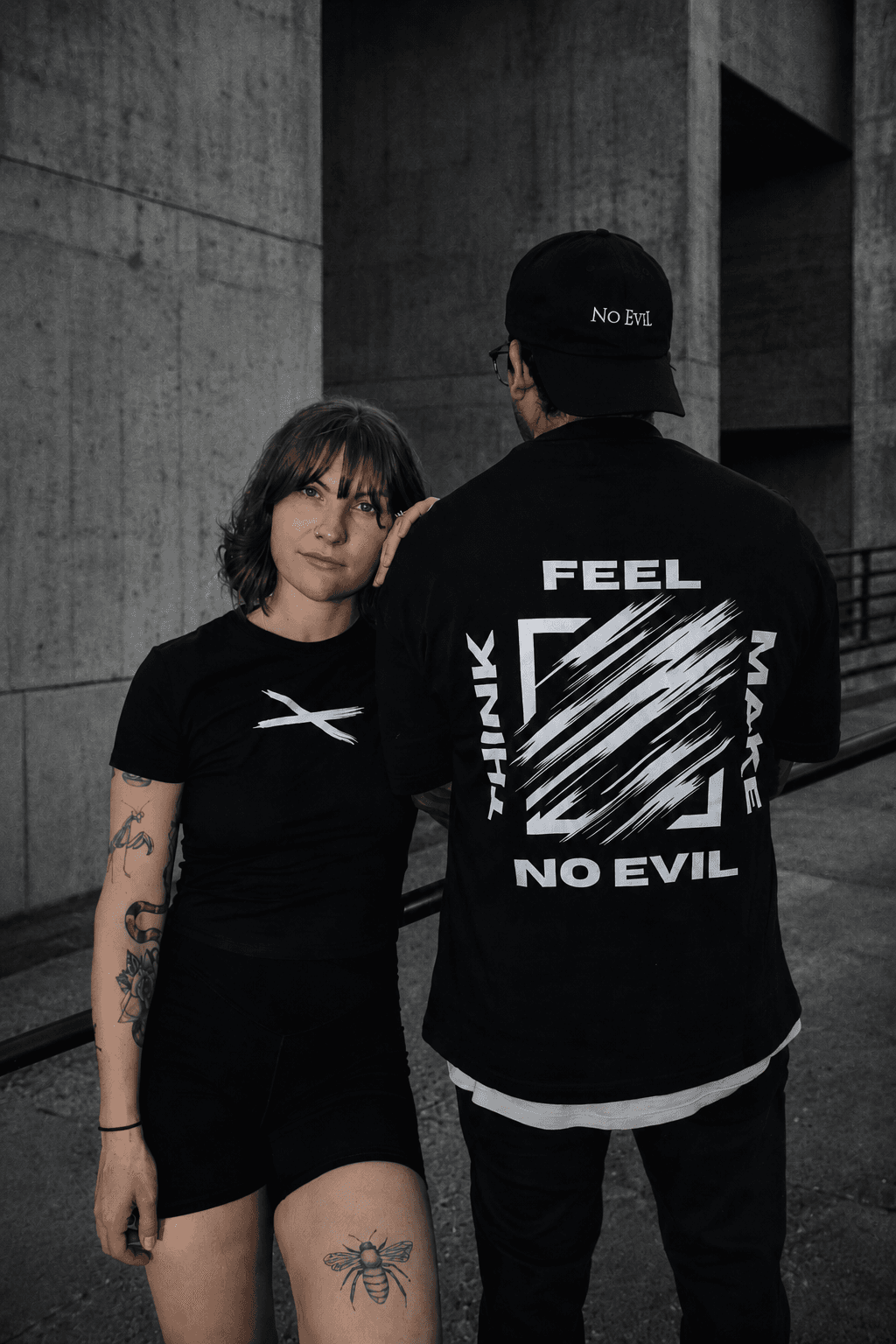 Two models in No EviL graphic tees posing in front of brutalist concrete architecture